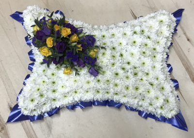 Based Pillow - At Sarah Coxon Floral Design we are delighted to present this product available for flower delivery in Mid and North Norfolk. 

A based pillow is a traditional funeral tribute, it is based in white Chrysanthemums, and is edged in hand pleated ribbon in a colour co-ordinating waterproof ribbon. The spray of flowers on top of the pillow is raised above the Chrysanthemums and includes a beautiful selection of Roses, spray Carnations and other flowers to complement the design. 

The flowers are arranged in water retaining foam (oasis) to ensure maximum freshness. 

Standard - approx 12" x 18"

Deluxe - approx 14" x 21"

Luxury - approx 17" x 24"

We deliver directly to all of the local funeral directors and will contact them to confirm a delivery time. 

Our flowers at Sarah Coxon Floral Design arrive fresh from the Dutch auctions every day so you can be rest assured we are using the best quality of flowers available. 

If you would like to choose a colour scheme, please state this in the special request box. Suggested colour schemes are red and white, yellow and white, pink and white and peach and white. If no colours have been selected we will use the same colours as the picture.